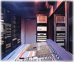 薄青紫色のライトの部屋に音響設備やコンピュータが並ぶ機械室の写真