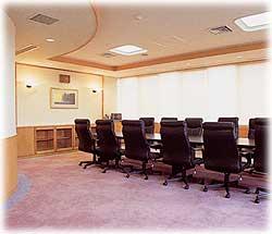 紫色の絨毯が敷かれ、中央には長い机、その周りには背もたれの高い高級感のある椅子が並んでいる、大企業の重役クラスが会議をする場所のような健康総合相談室の写真
