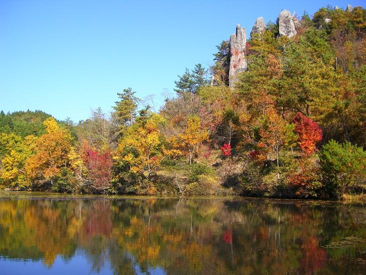 赤や黄色に色づいた木々と高くそびえる岩峰、その景色が水面に映っている写真
