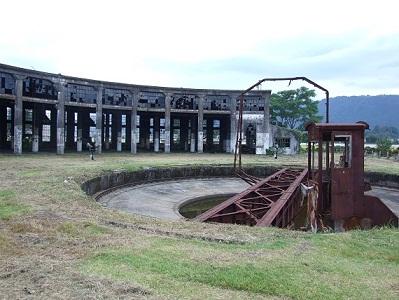 奥に扇型機関庫の建物があり、手前に一段低く円形の中央に錆びれた転車台の写真