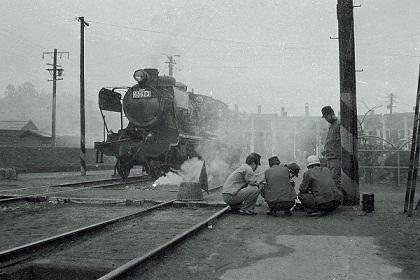 奥に煙に霞んだ旧豊後森機関庫があり、手前に5名の作業員が座っている左側に走ってきている機関車の古写真