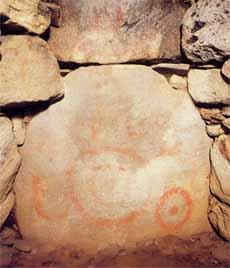 川原石で覆われた墳丘の石に、赤色で人の顔のようなものが描かれている鬼塚古墳の写真