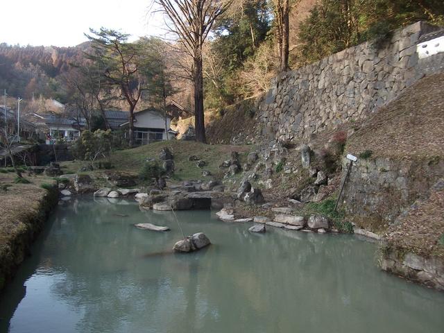 石塀で囲われた山の下の堀に、形の違う石組が配置されている清水御門御茶屋庭園の写真
