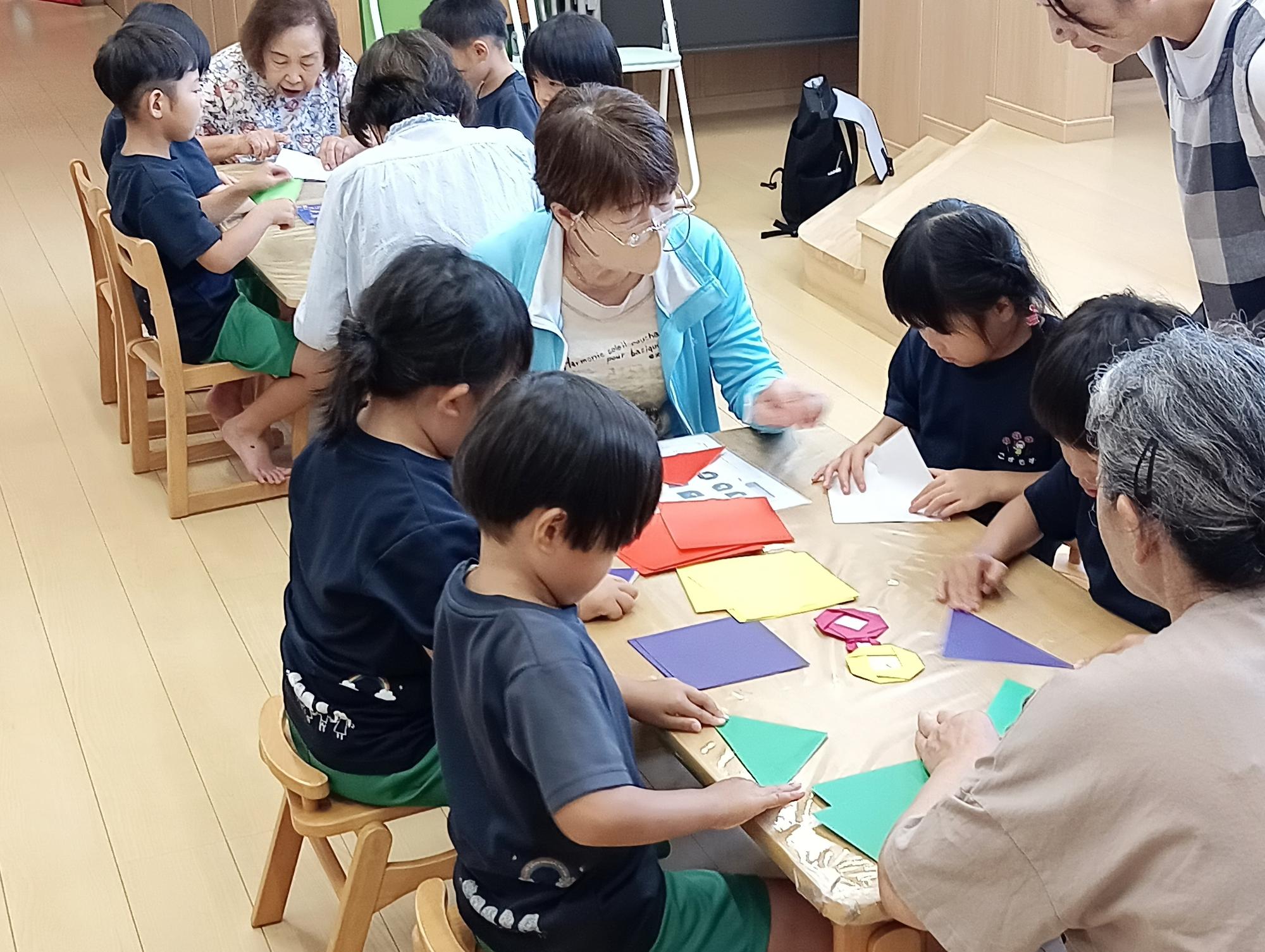 折り紙わらべのみなさんが保育園の子どもたちにおりがみを教えている写真