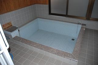 灰色の床タイルで水色のタイルの浴槽がある憩いの湯の女湯を入口から見た写真