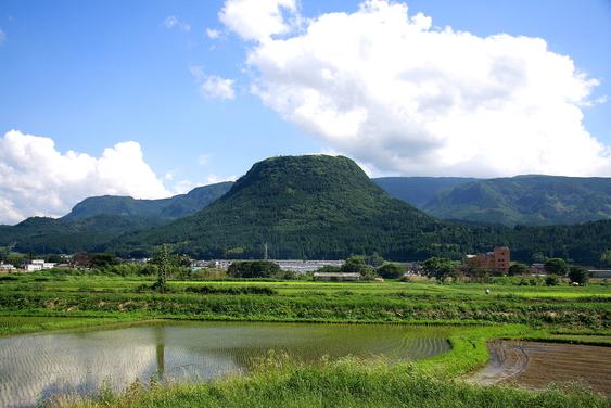 青空に白い雲の中、手前に田んぼが広がり、その奥に緑の伐株山（きりかぶさん）がみえその奥に広大な山々が並んでいる風景写真